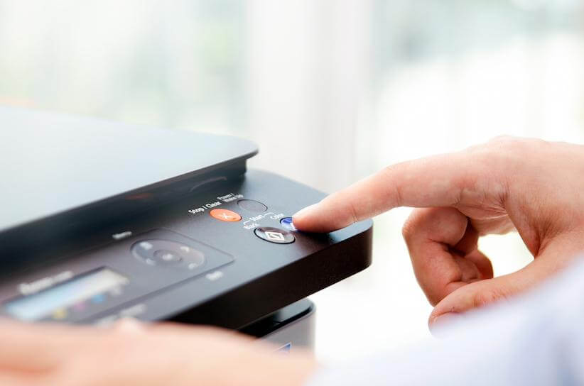 shutterstock_730017487 factory reset a printer to wipe data close up of a light skinned person pressing a button on the top of a printer