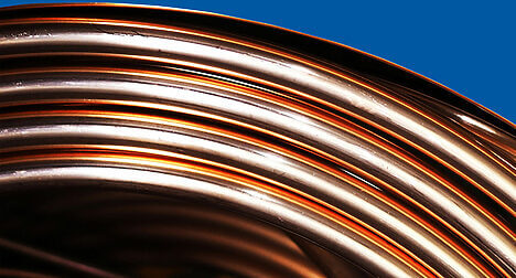 a close up of a roll of copper pipe curved across the image against a blue background