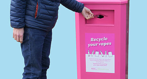 light skinned man putting a vape in to a bright pink recycling bin for vapes