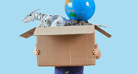 a child holding a large cardboard box full of toys, it covers their face entirely