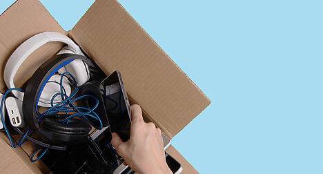birds eye view of a cardboard box full of old electricals, a light skinned hand taking one object out