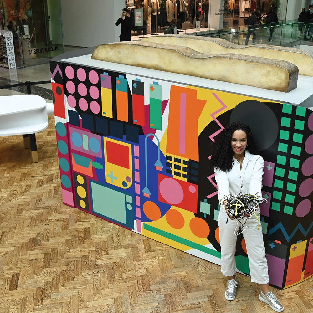 LoveYourToaster page 2024-Header-image dark skinned presenter Michelle Ackerley in front of giant multi-coloured patterned toaster in a shopping centre, holding a handful of cables